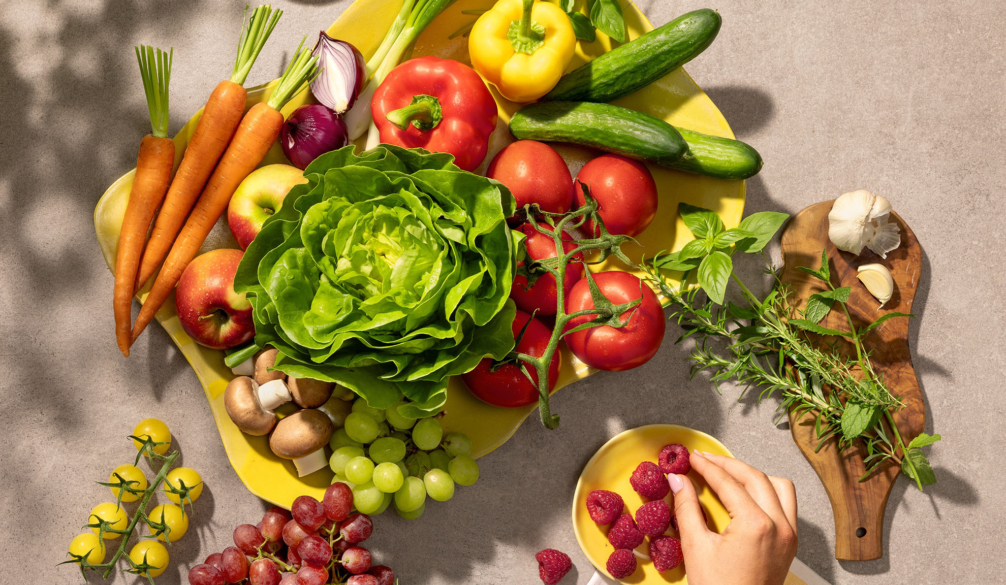 Fresh vegetables and fruits on a yellow platter, including carrots, lettuce, bell peppers, tomatoes, and grapes.