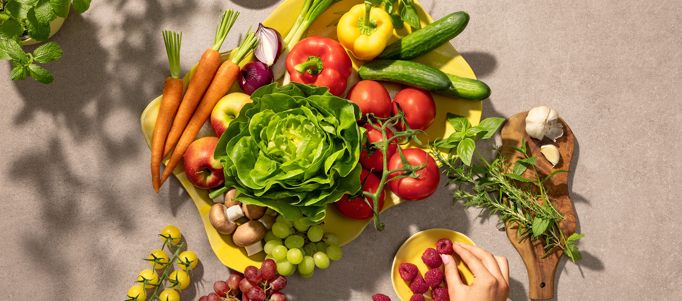 Fresh vegetables and fruits on a yellow platter, including lettuce, tomatoes, carrots, and berries.