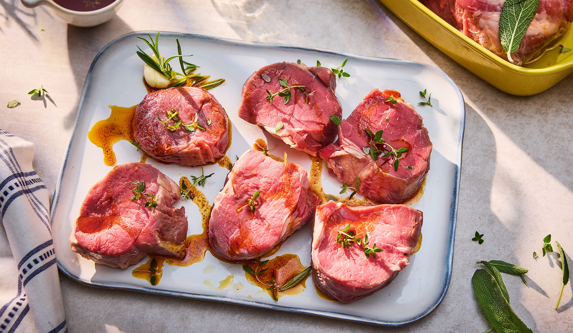 Raw beef medallions with herbs and oil on a white platter