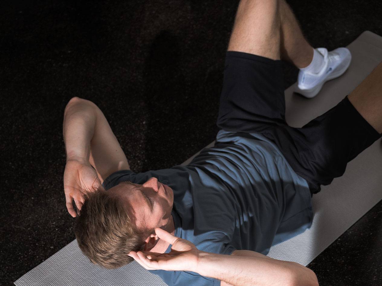 Man in blue t-shirt and black shorts doing crunches on a yoga mat.