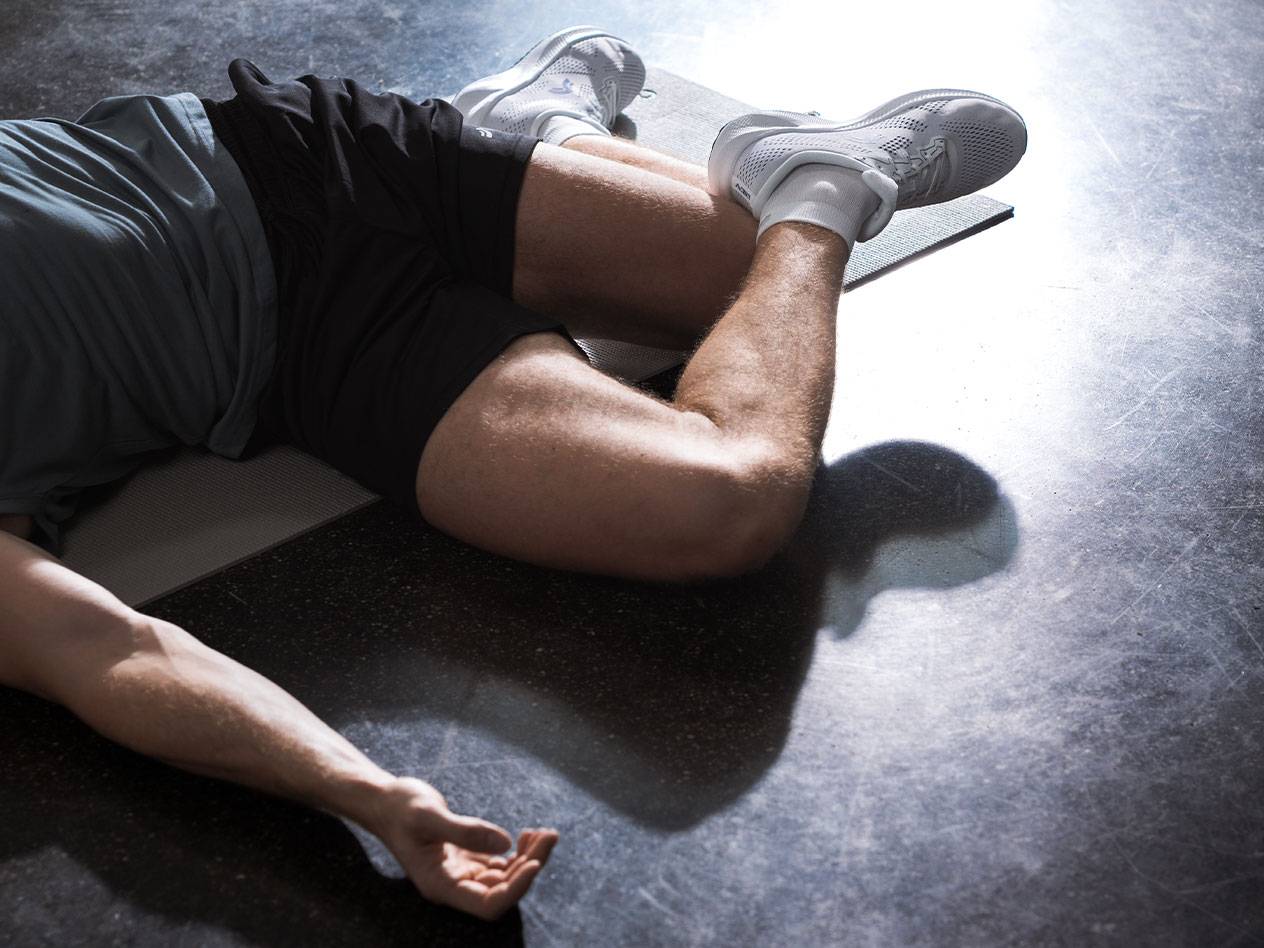 Man lying on a gym mat in athletic apparel and shoes.