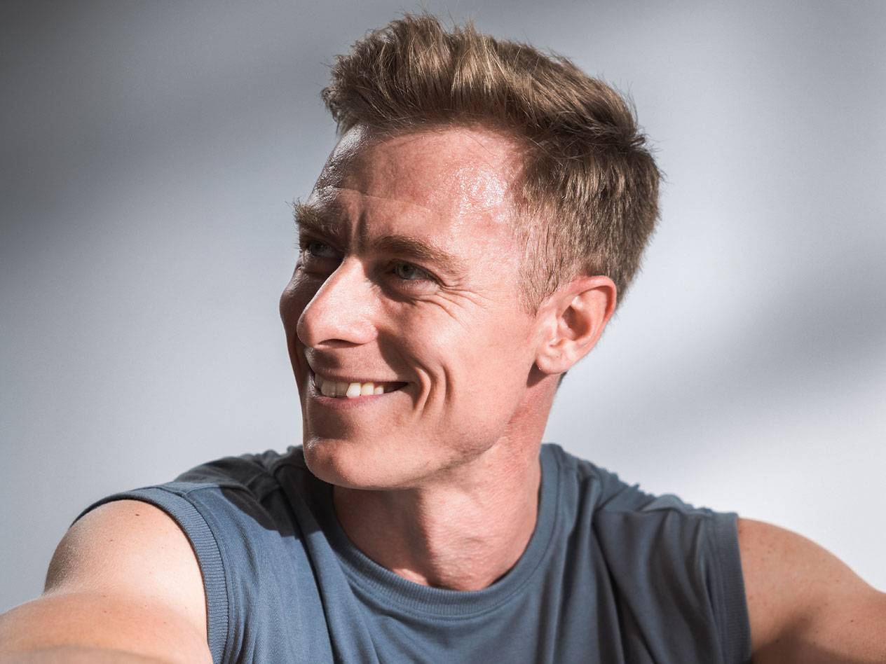 A smiling man with short hair and a sleeveless shirt.