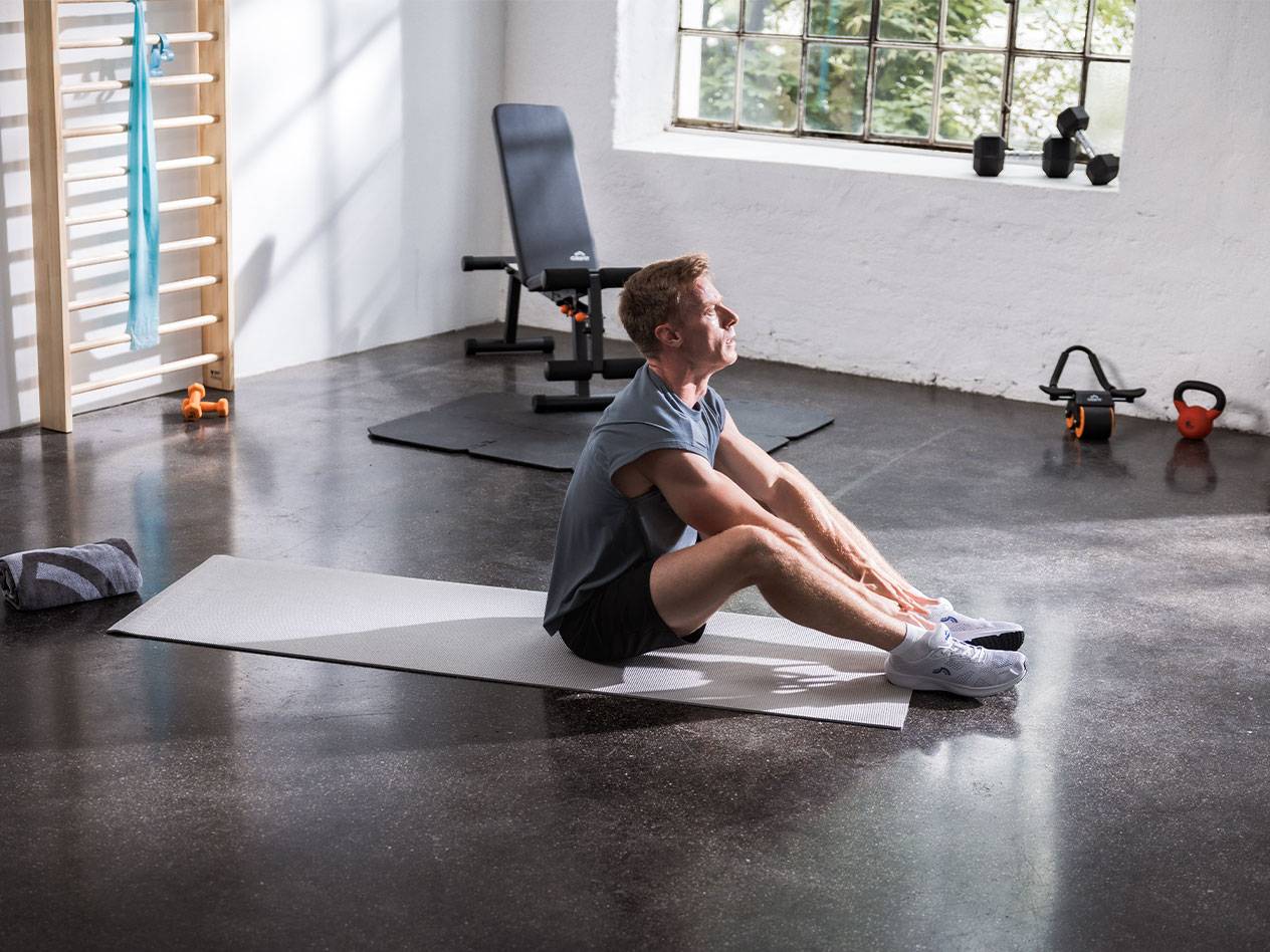 A man stretches on a yoga mat in a gym with equipment.