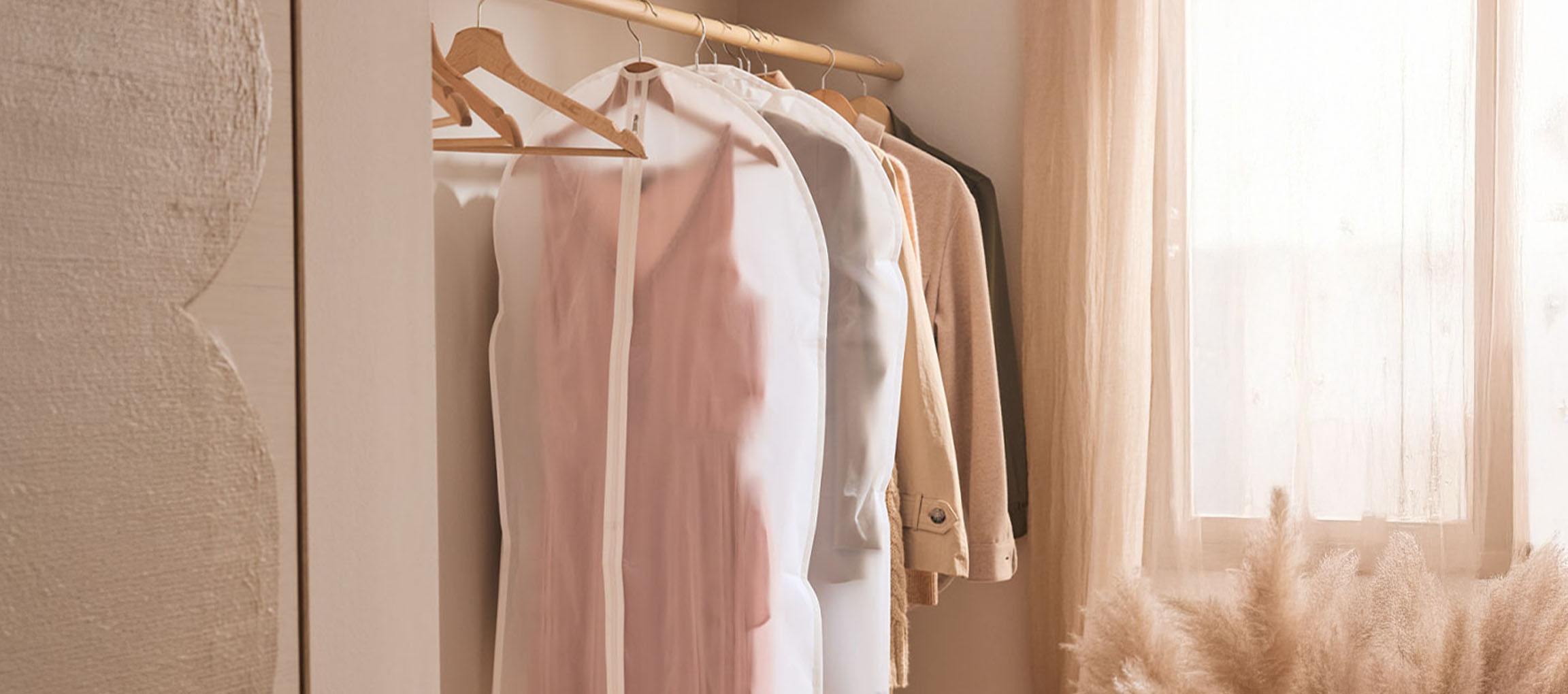 Garment bags and clothes on hangers in a closet by a window.
