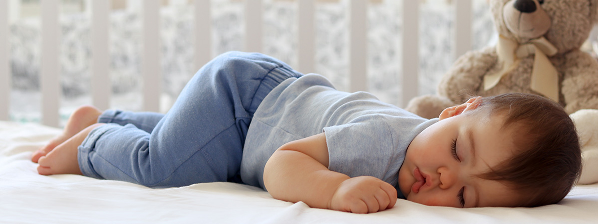 Sleeping baby in blue pajamas, beside a teddy bear.