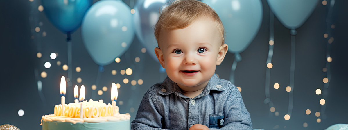 Baby smiles at birthday cake with candles and blue balloons.