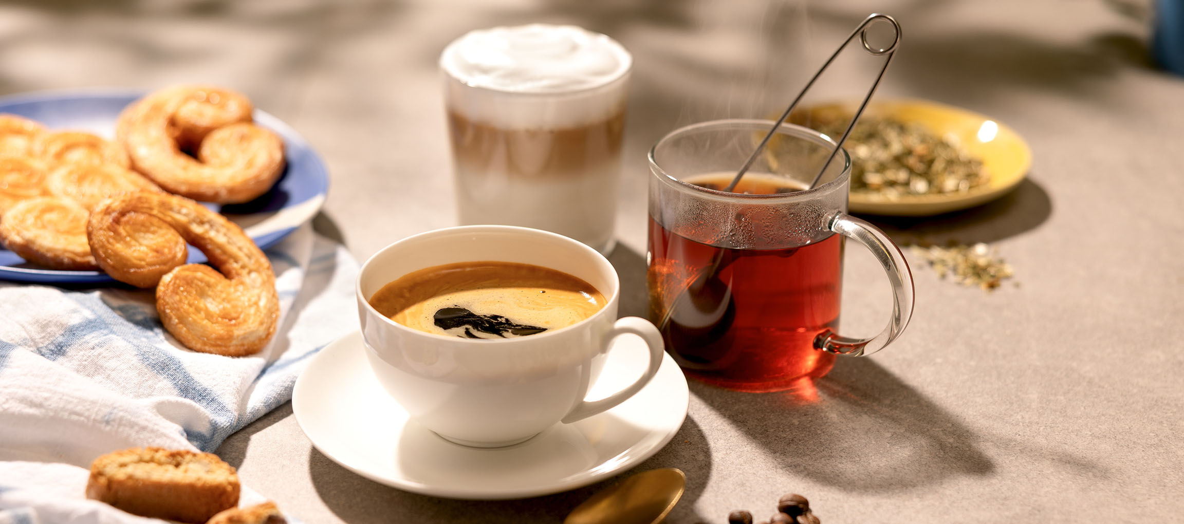 Coffee, latte, and tea with pastries on a sunlit table.