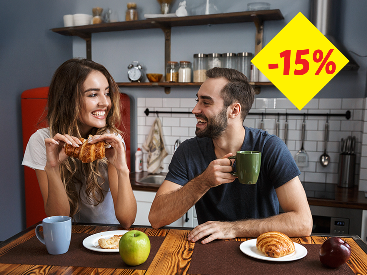 A couple enjoying breakfast with croissants and coffee in a kitchen, with a -15% discount sign.