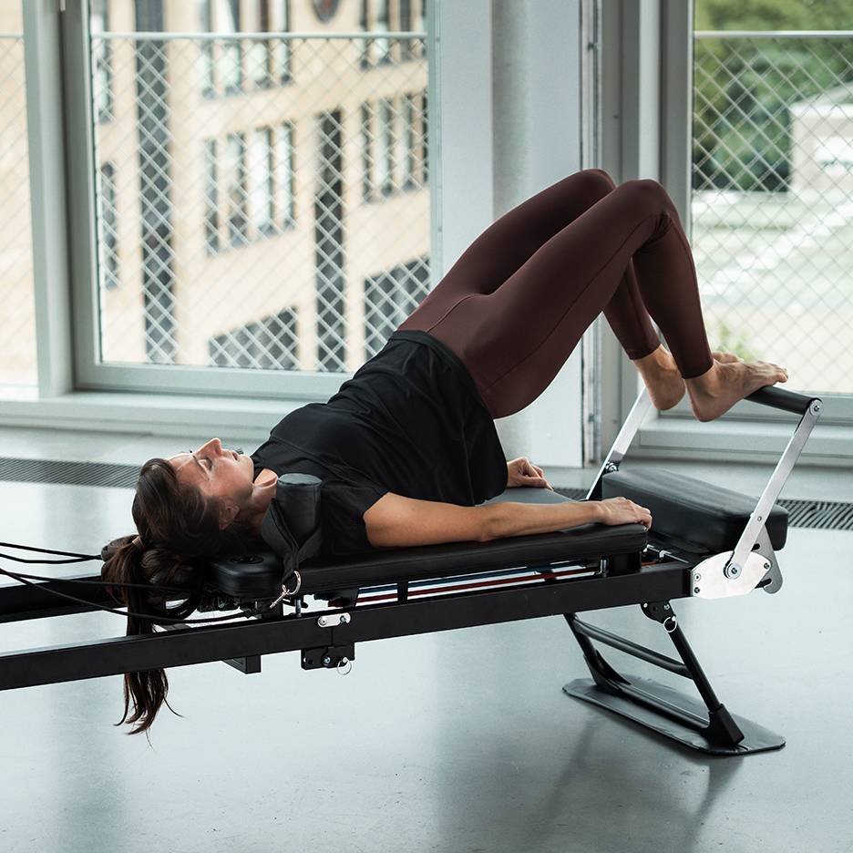 Woman exercising Pilates on a reformer machine, legs up.