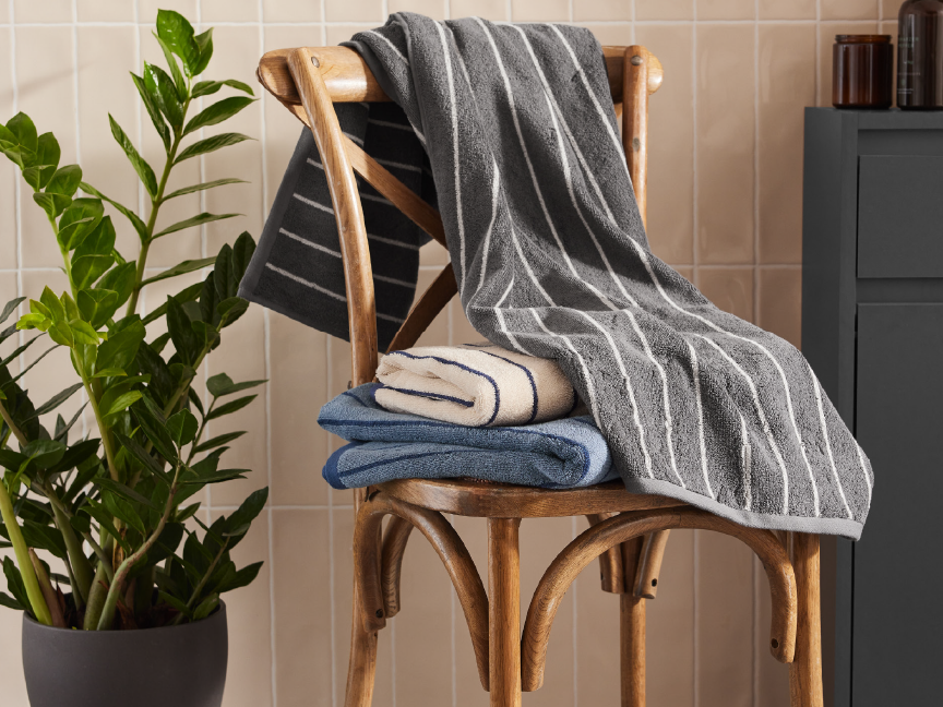 Striped bath towels neatly stacked on a wooden chair in a bathroom setting.