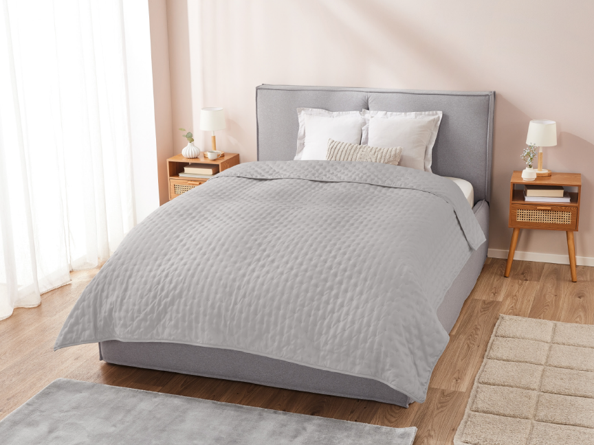 A modern bedroom with a grey upholstered bed, light grey quilted bedspread, and wooden nightstands.