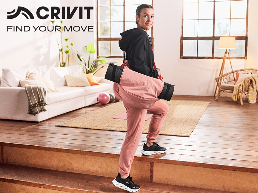 Woman in activewear carrying a yoga mat and bag, walking up steps in a bright home.
