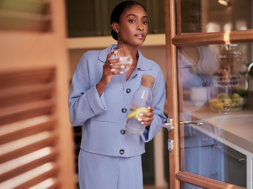 A woman in a blue outfit holds a glass of water and a bottle of lemon water.