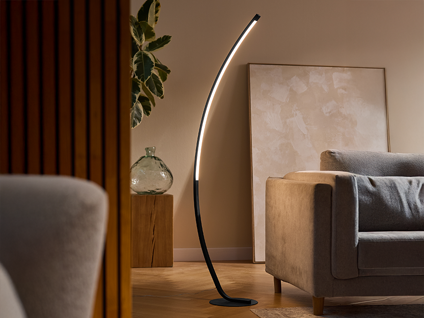 A modern black floor lamp with a curved LED light strip illuminates a living room.