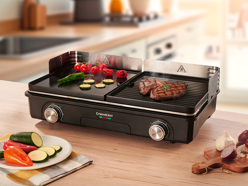 A SilverCrest electric grill with cooking vegetables and steaks on a wooden table.