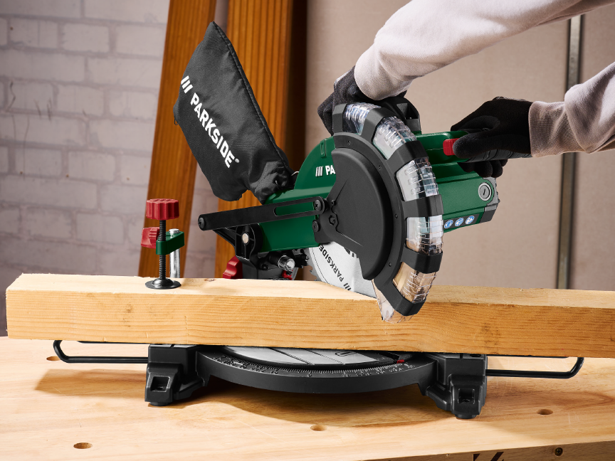 A person using a Parkside miter saw to cut a wooden beam.