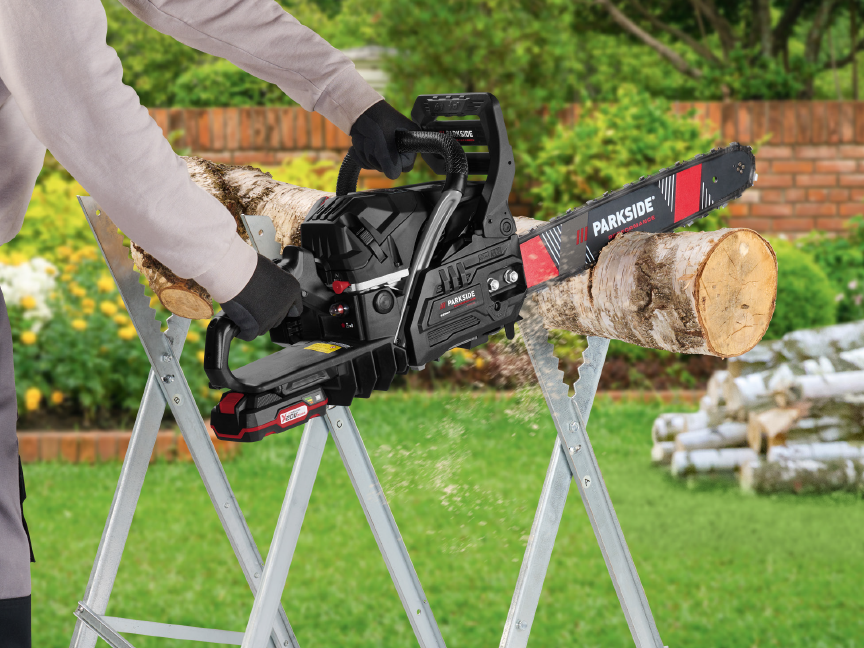 A person using a Parkside chainsaw to cut a log on a sawhorse in a garden.