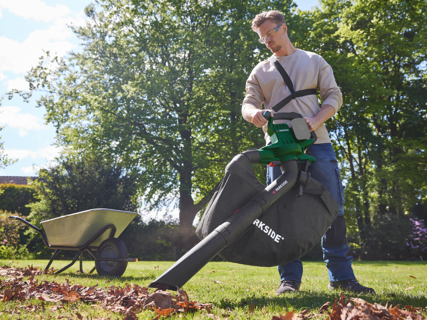 Man using a Parkside leaf blower/vacuum to clear leaves from a lawn.