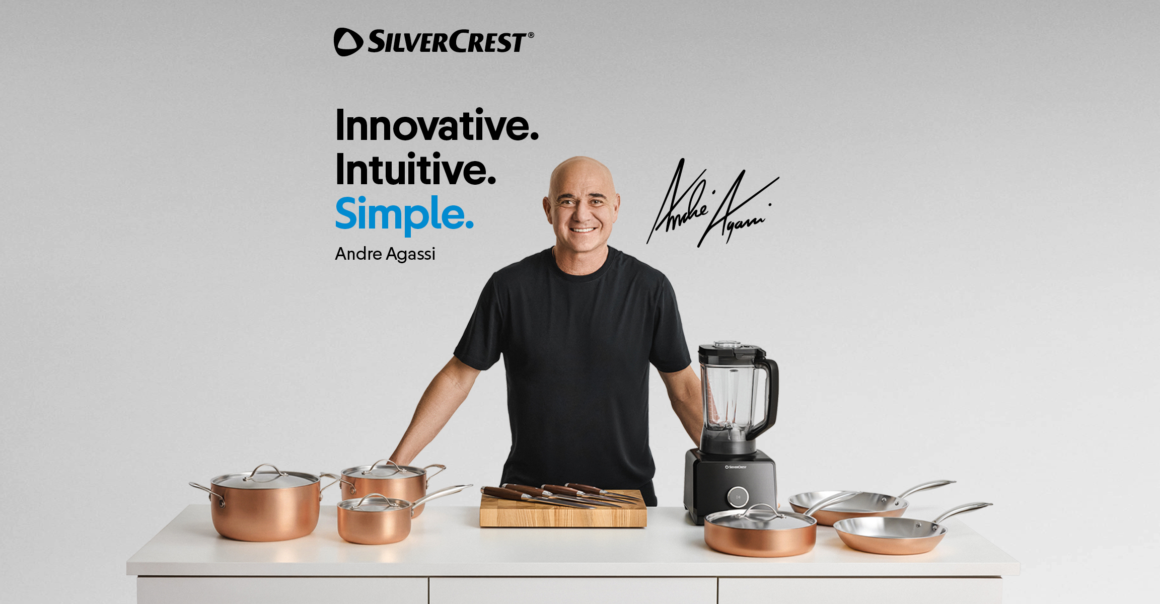 A man presenting a kitchenware collection with copper pots, pans, knives, and a blender.