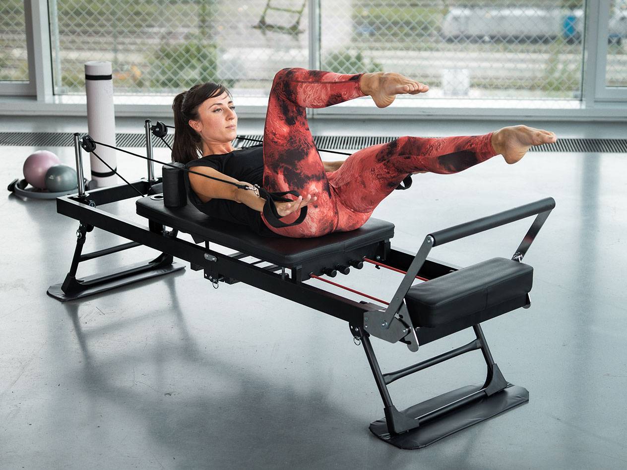 Woman exercising Pilates on a black Pilates machine with red details.