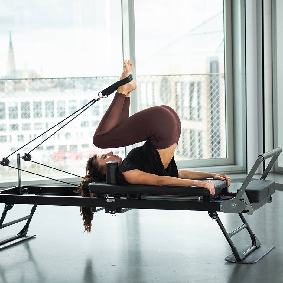 Woman doing Pilates on a reformer with legs up and feet in straps.