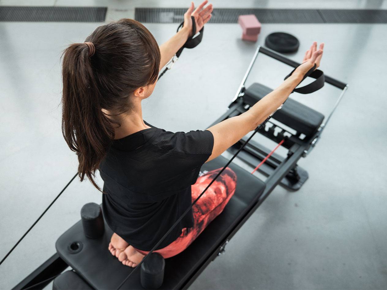 Woman exercising Pilates on a reformer machine with resistance bands.
