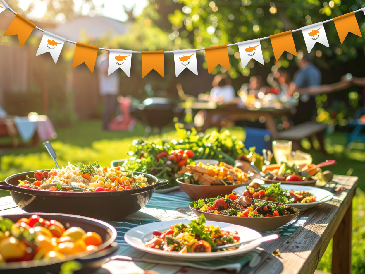 Festive outdoor table setting with Cypriot flags and abundant Mediterranean food.