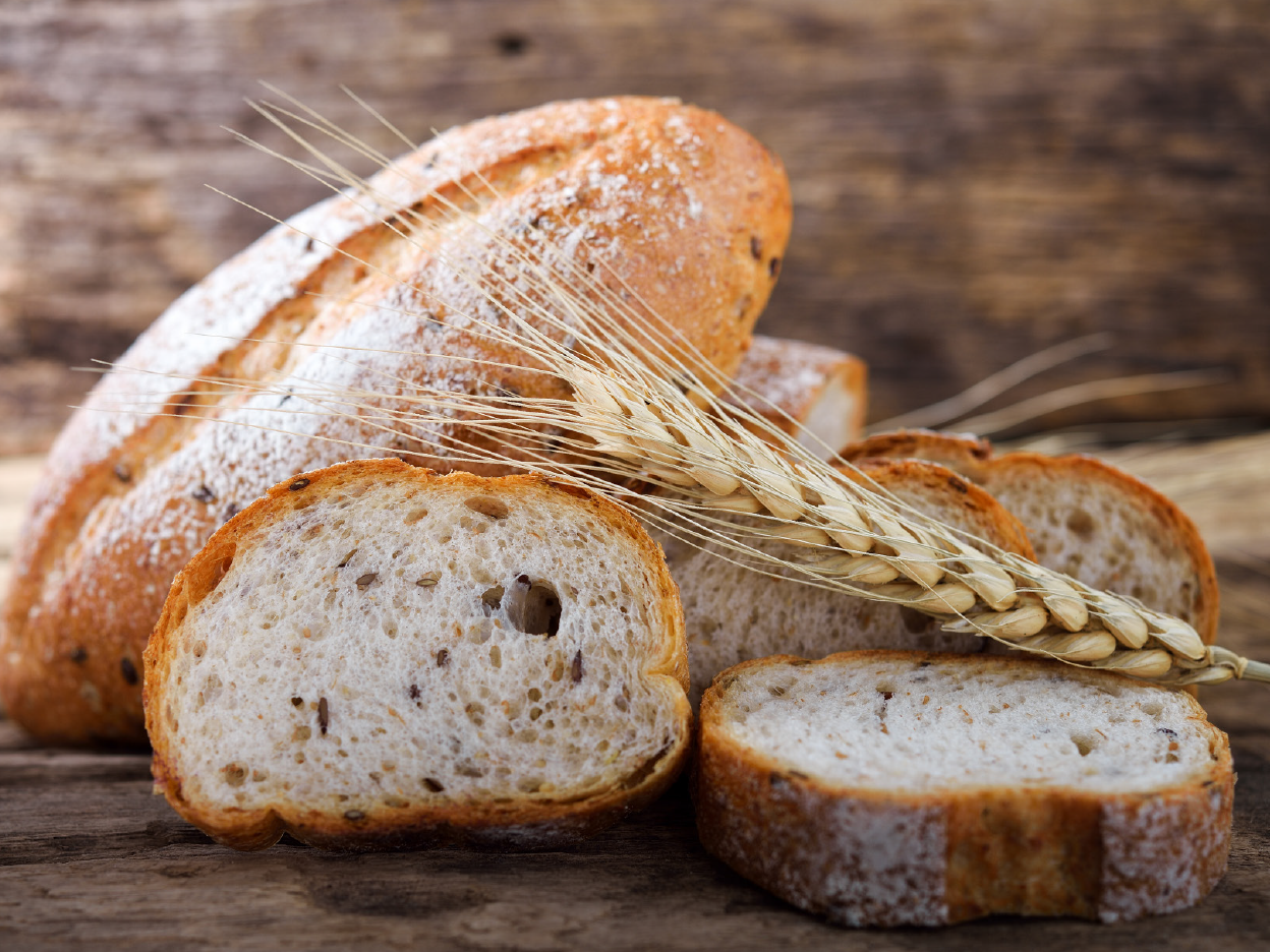 Sliced bread with seeds and wheat stalks on a wooden background.