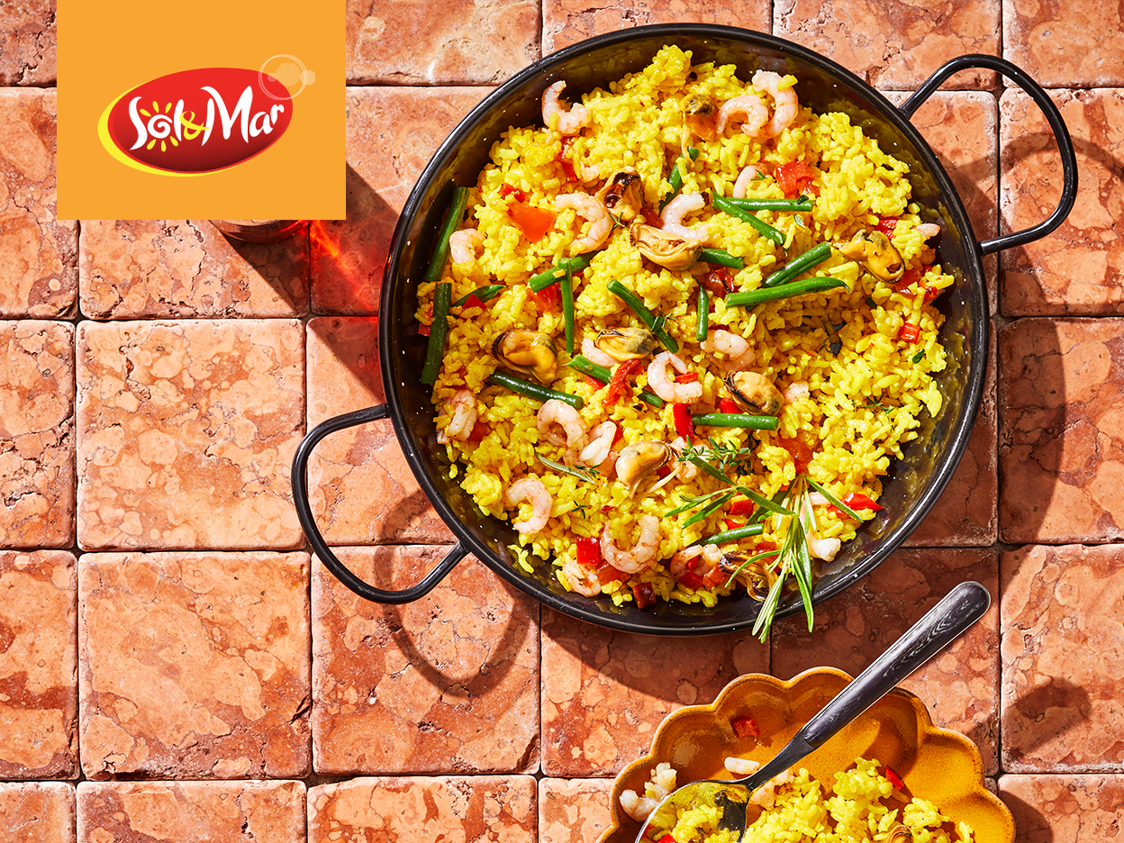 A paella pan filled with seafood paella, next to a bowl of paella and the Sol&Mar logo.