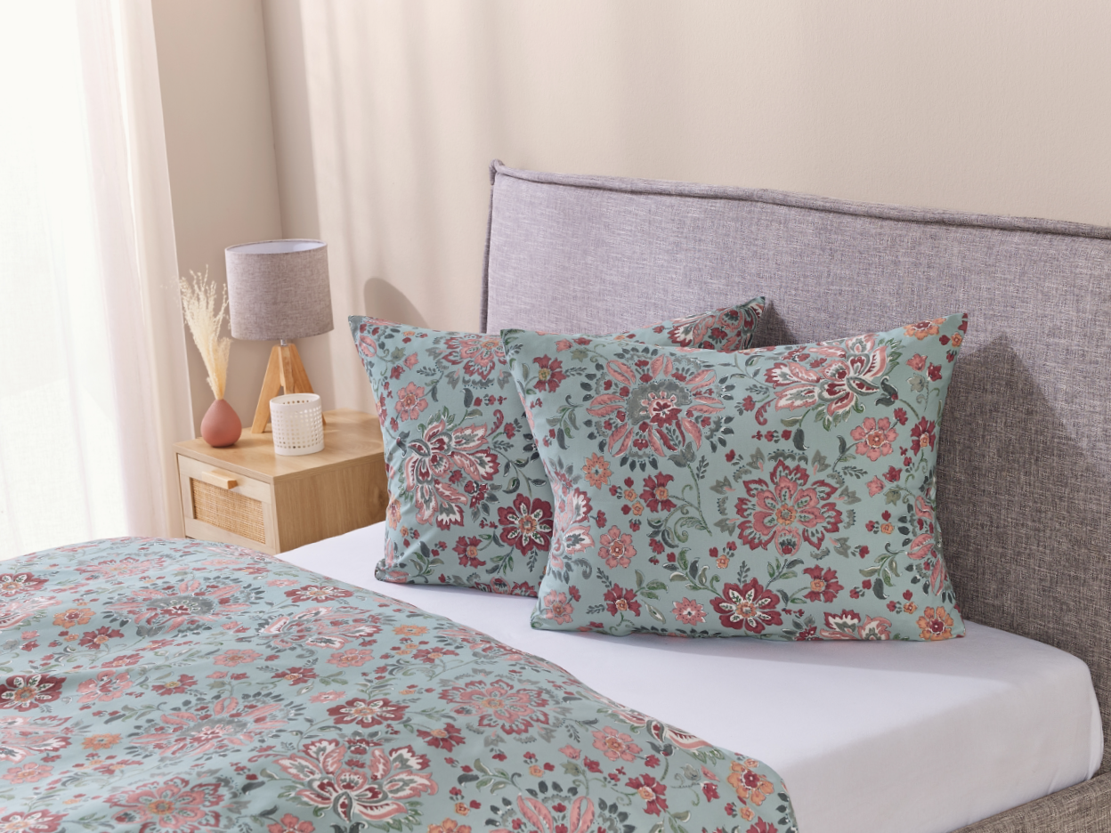 A bed with a gray headboard, light blue floral duvet cover, and two matching pillows.