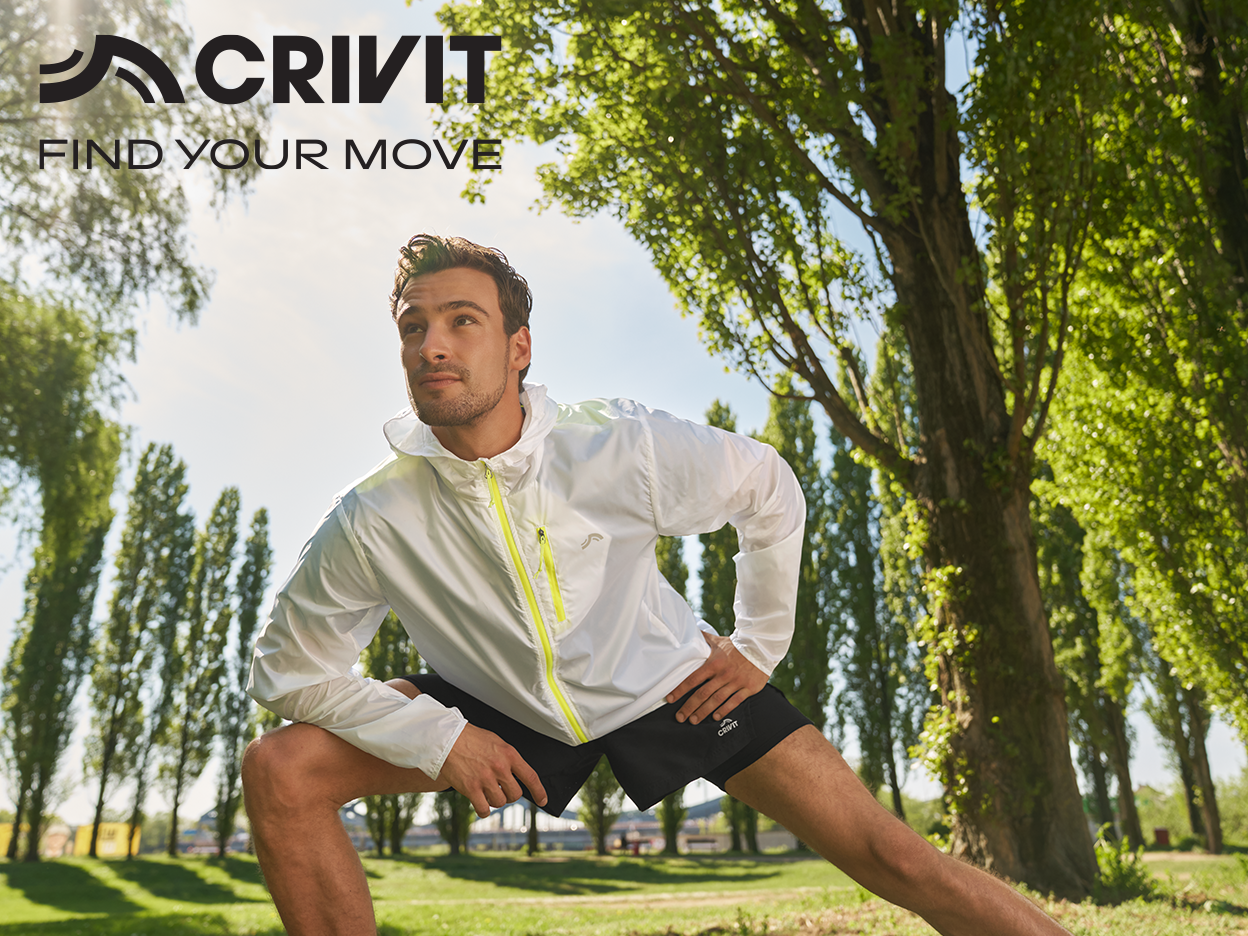 Man in white Crivit sports jacket and black shorts stretching outdoors.