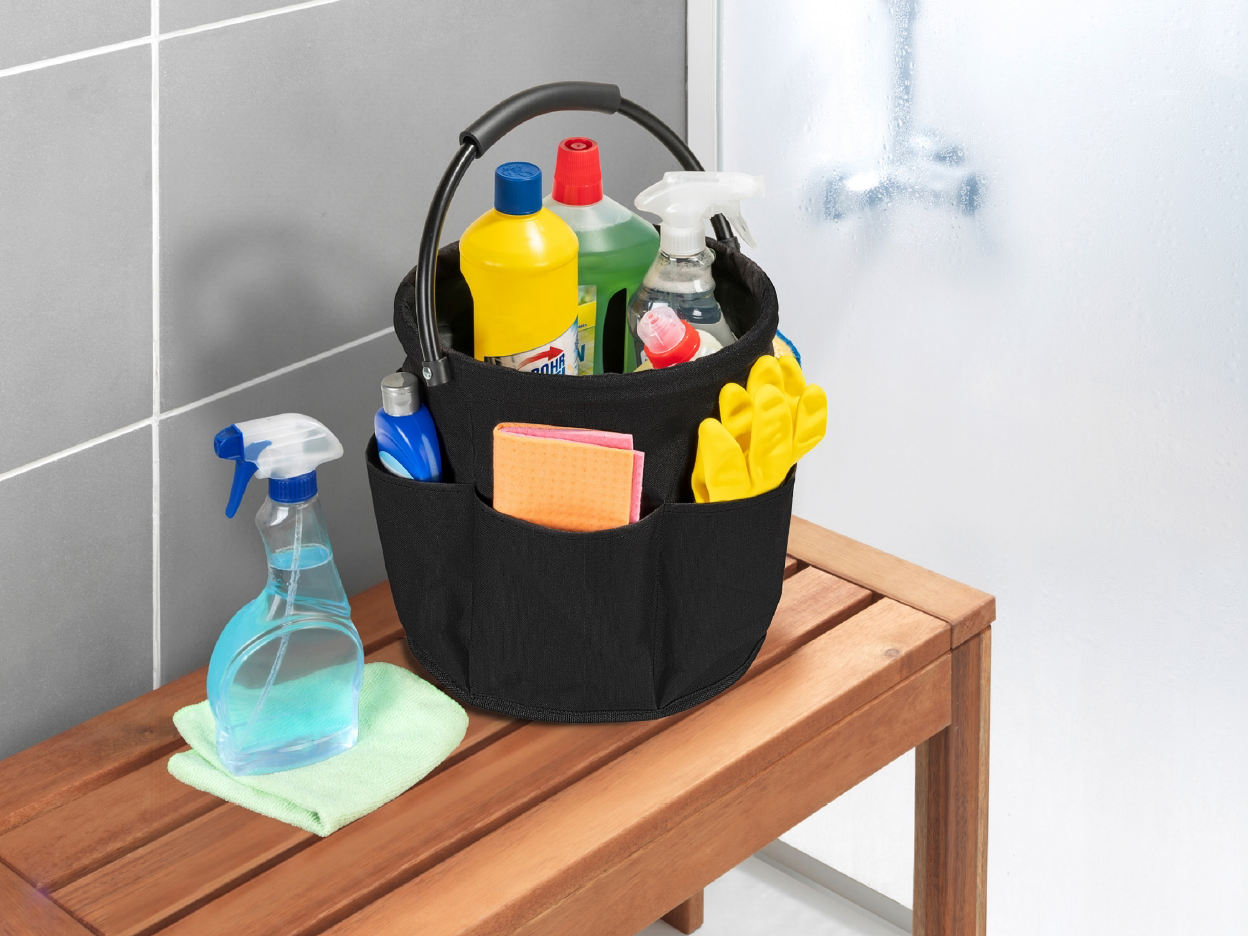 Black cleaning caddy with various cleaning supplies on a wooden bench.