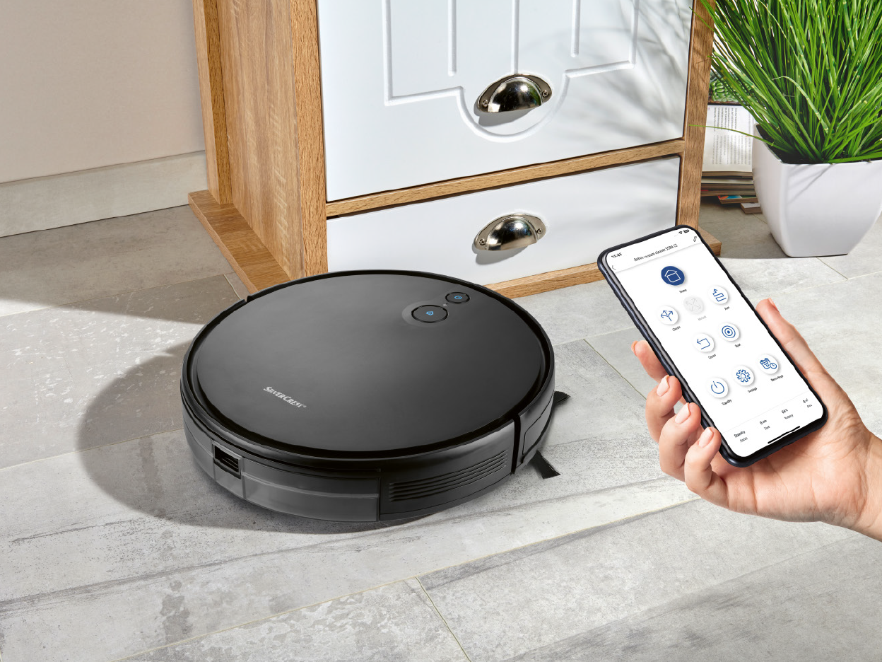 A robotic vacuum cleaner on a tiled floor, controlled by a smartphone app.
