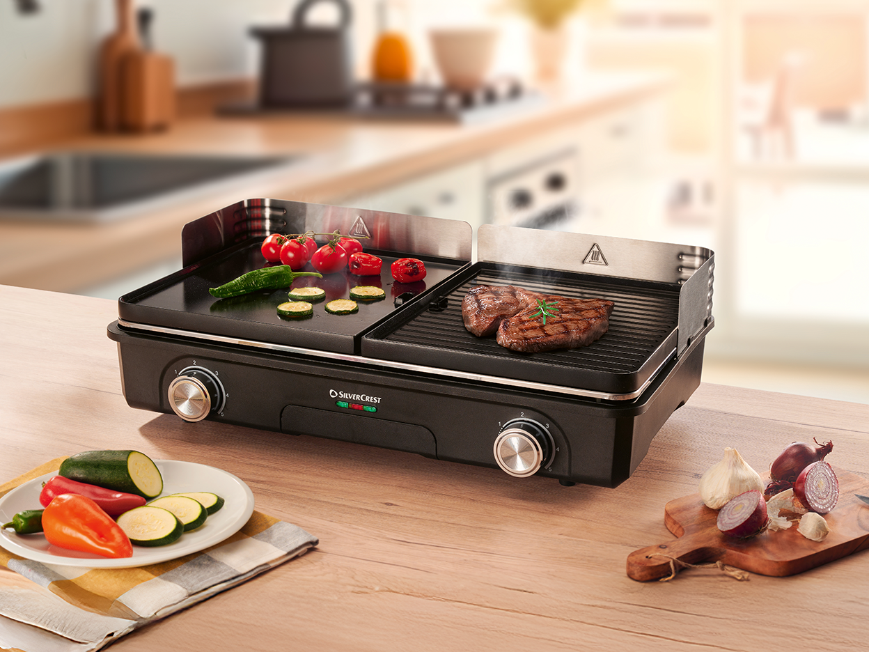 SilverCrest electric grill with steak and vegetables cooking on a kitchen counter.