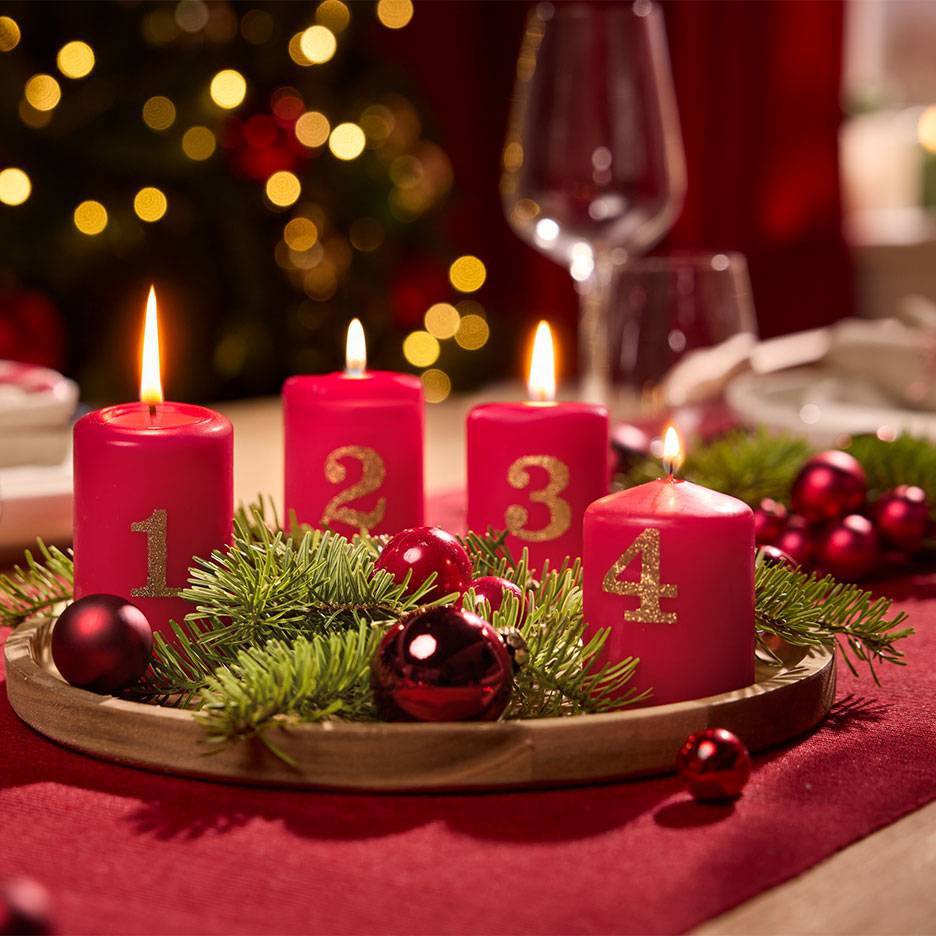 Advent wreath with four red candles numbered 1 to 4, surrounded by fir branches and baubles.