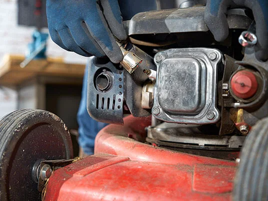 Χέρια με γάντια αντικαθιστούν το μπουζί σε ένα κόκκινο χλοοκοπτικό.