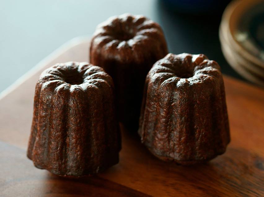 Three canelés de Bordeaux on a wooden board.