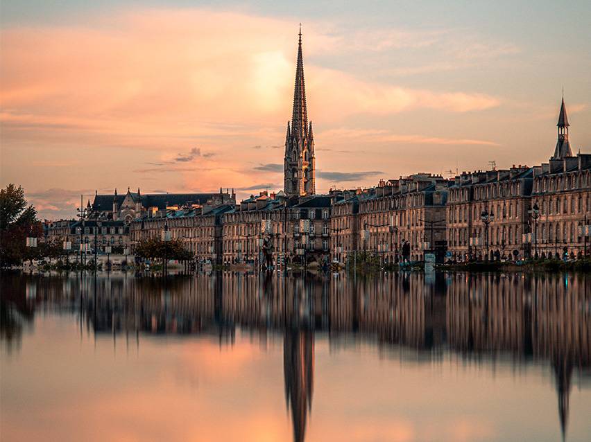 Bordeaux cityscape at sunset with a church and its reflection in the water.