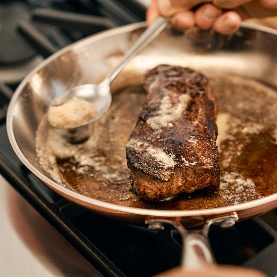 A steak is cooking in a pan with butter being basted over it.