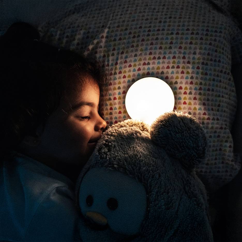 Girl sleeping with a plush toy and a glowing night light.