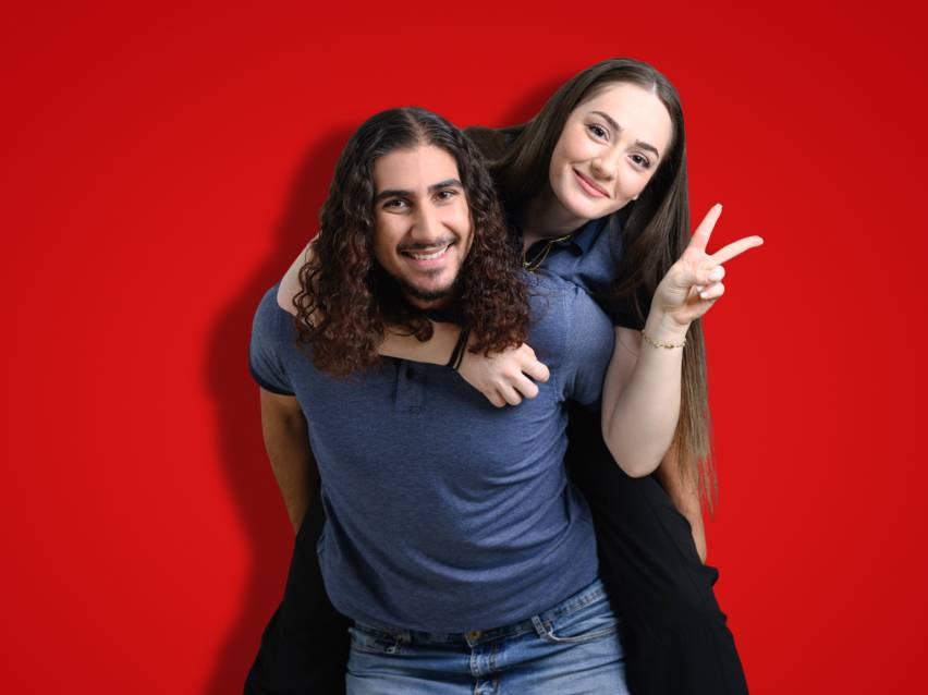 A man giving a piggyback ride to a woman, both smiling and wearing casual clothes.