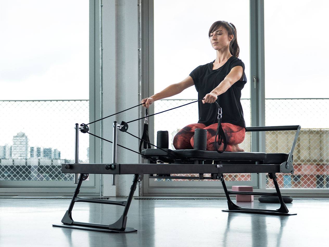 Woman doing Pilates exercise on a reformer machine with a city background.