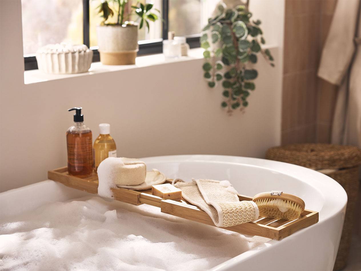 Bamboo bath caddy with bath products, sponges, and brushes over a bubble bath.