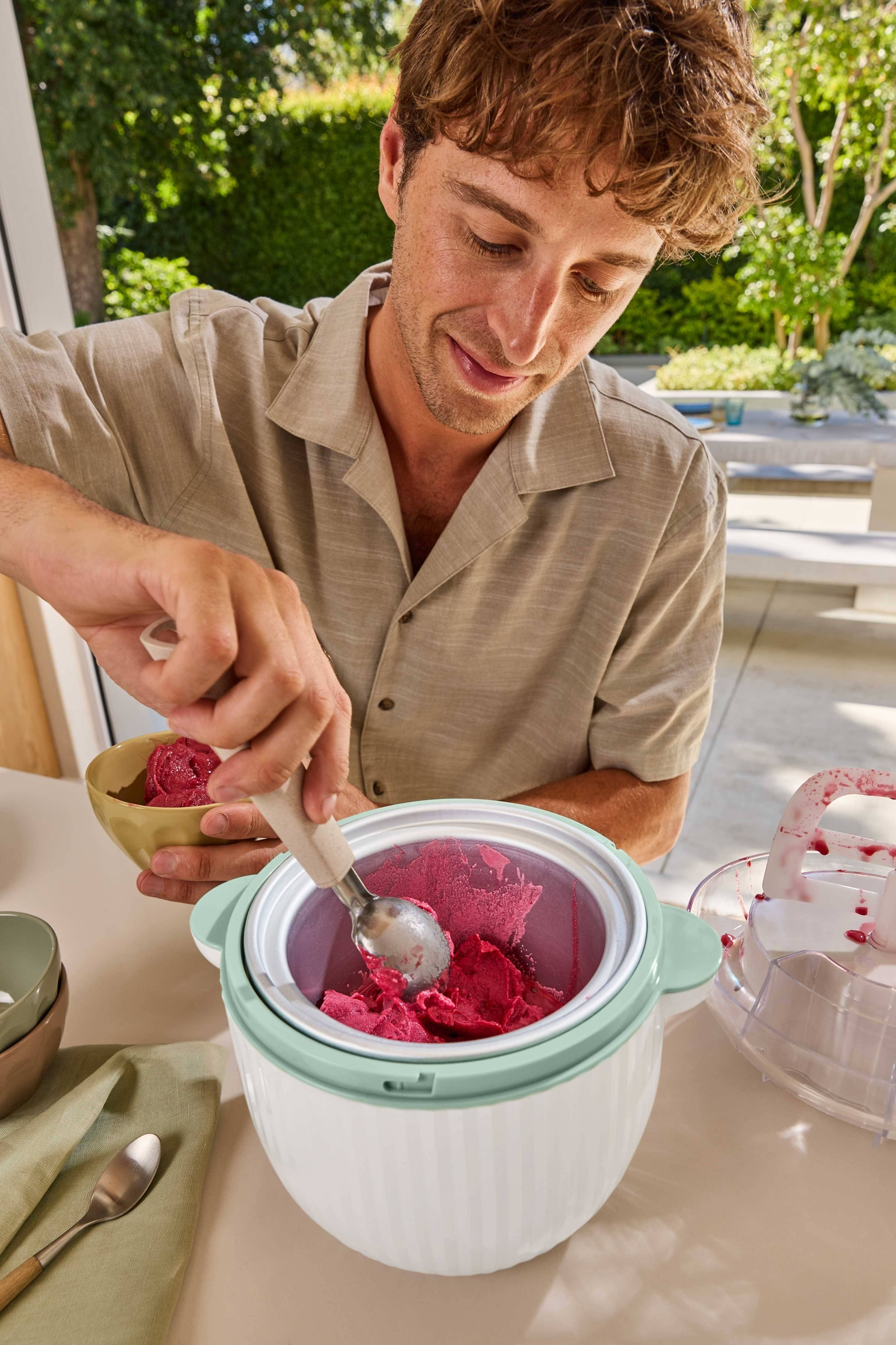 Man scooping red sorbet from an ice cream maker into a bowl.