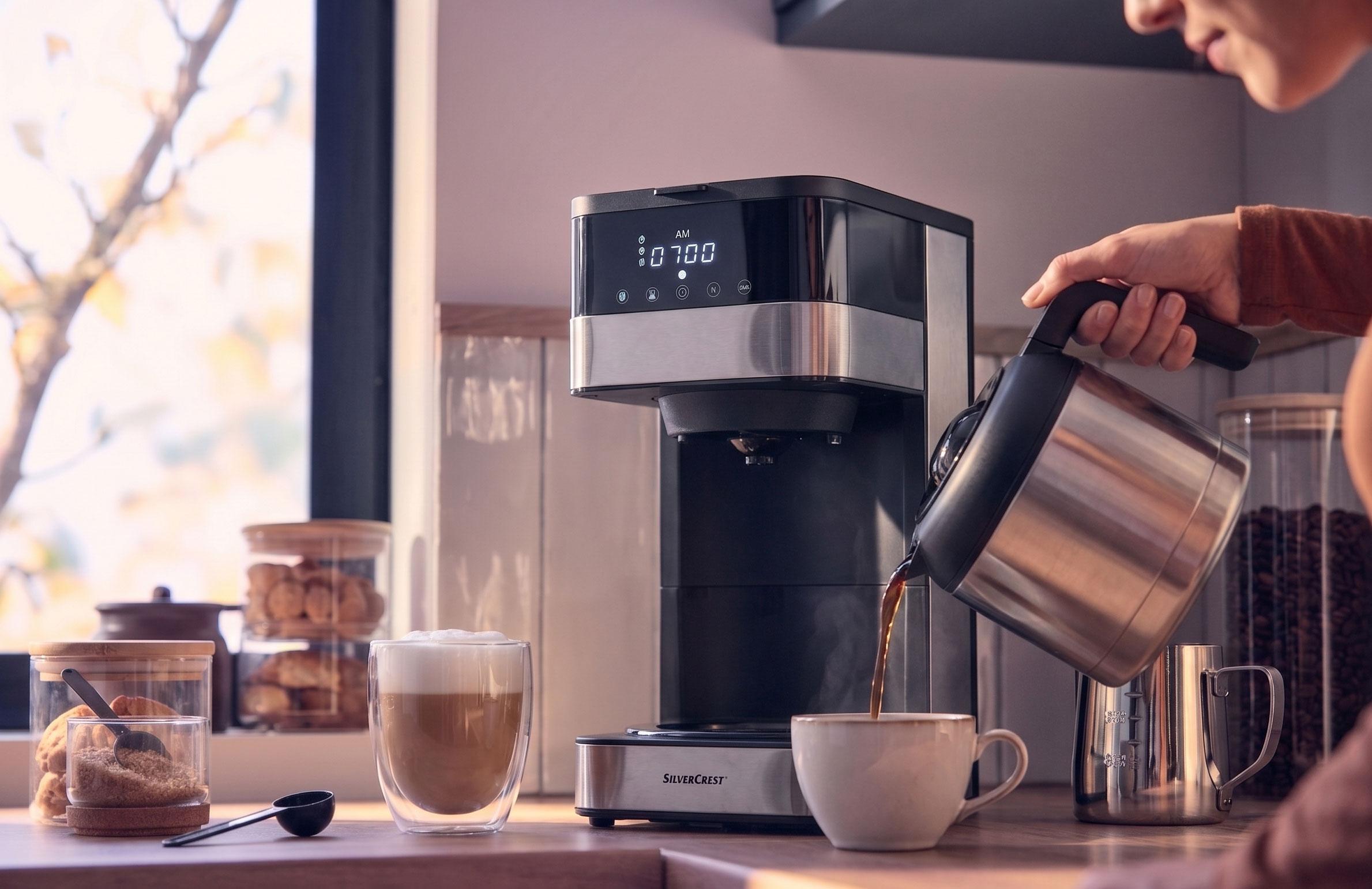 Coffee machine pouring coffee into a cup, with a latte and cookies on the counter.
