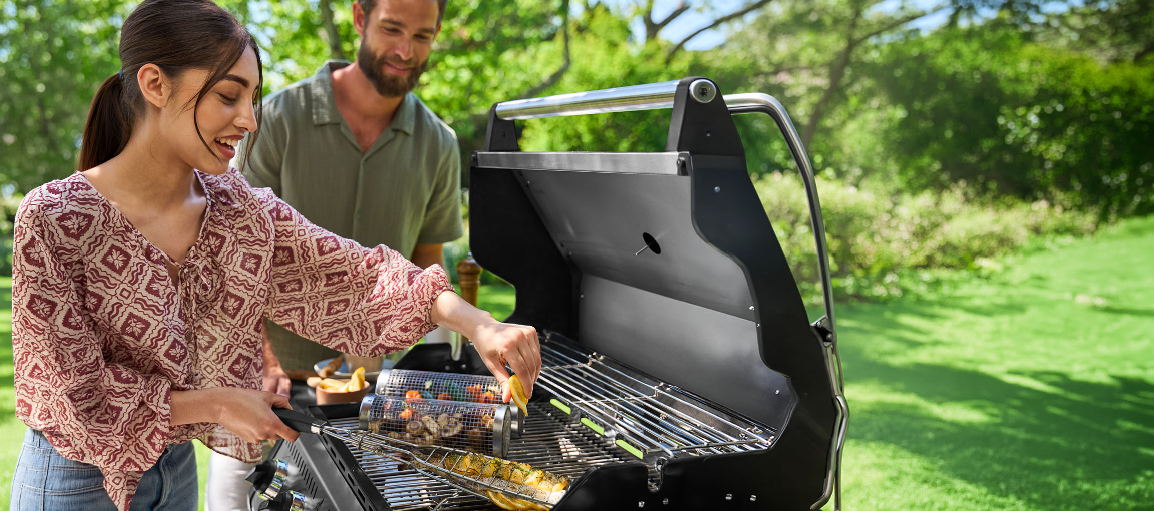 Couple grilling fish and vegetables on a barbecue in a sunny garden.