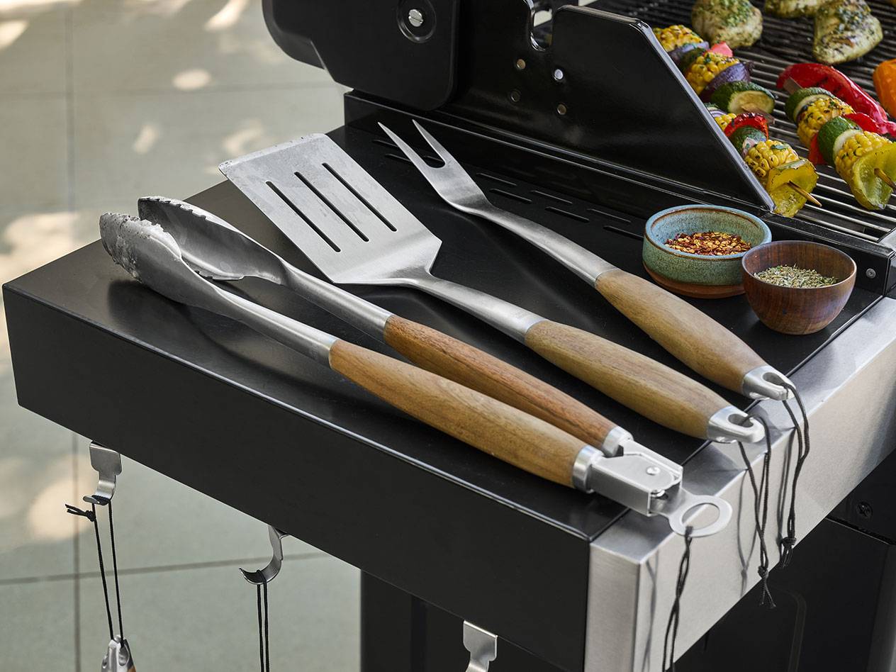 Barbecue tools with wooden handles and spices next to grilled vegetable skewers.