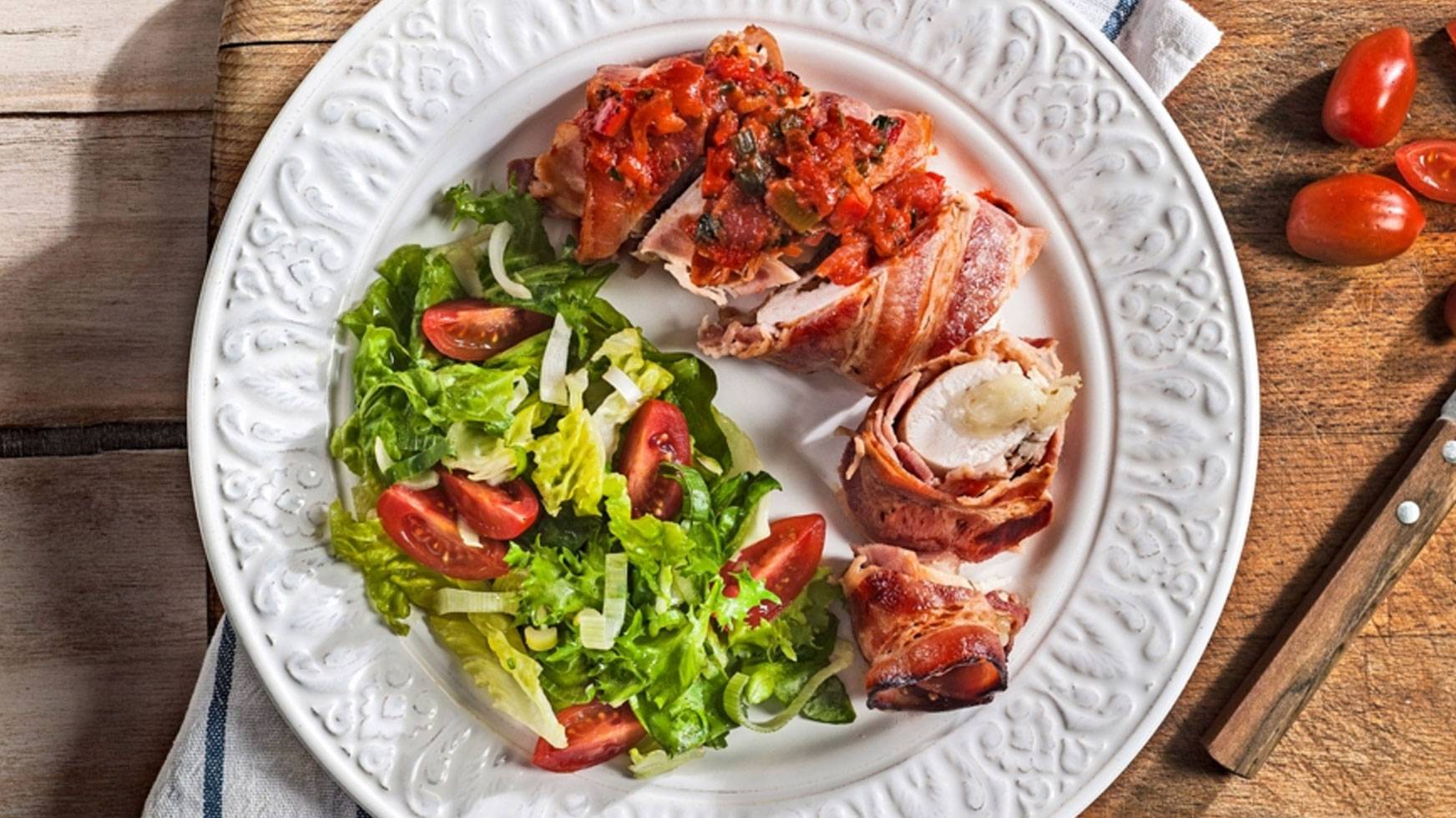 Κοτόπουλο τυλιγμένο σε μπέικον με σάλτσα ντομάτας και σαλάτα σε λευκό πιάτο.