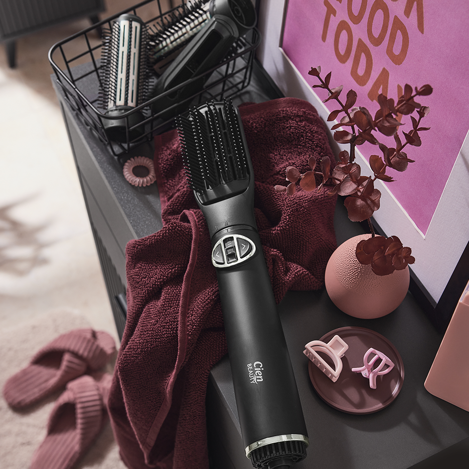 Συσκευή styling ζεστού αέρα Cien Beauty με αξεσουάρ, παντόφλες και διακόσμηση σε σκούρα επιφάνεια.