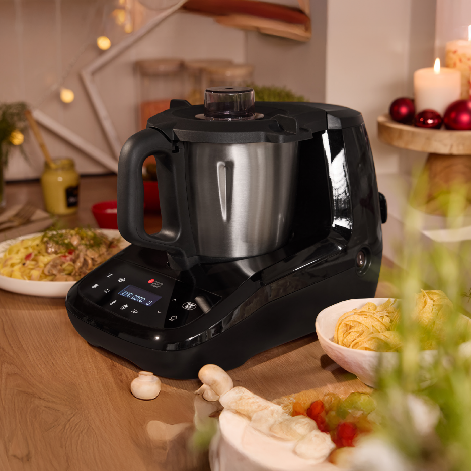 Black kitchen machine with a metal bowl on a wooden counter, surrounded by food and festive decor.